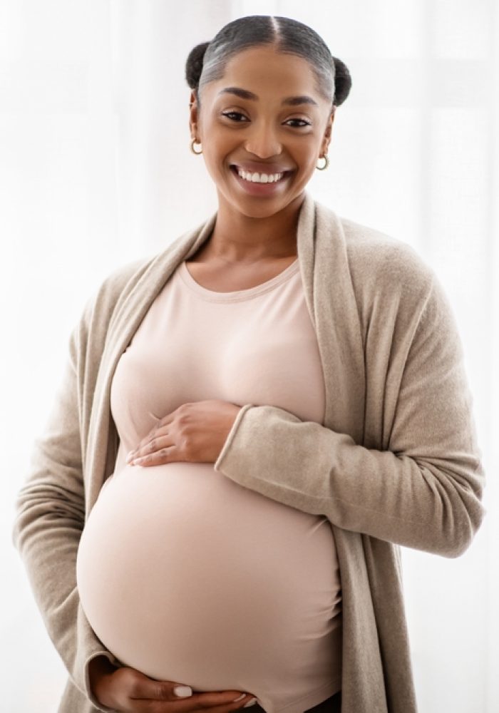 Happy,Black,Pregnant,Woman,Standing,Near,Window,At,Home,And